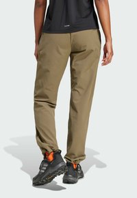 Khaki spodnie outdoorowe o luźnym kroju, z tapered leg. Połączone z czarnymi butami trekkingowymi z pomarańczowymi akcentami i solidną podeszwą.