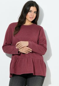 Sudadera burdeos con escote redondo, mangas largas y cintura de peplum. Textura suave y diseño casual, combinada con jeans oscuros.