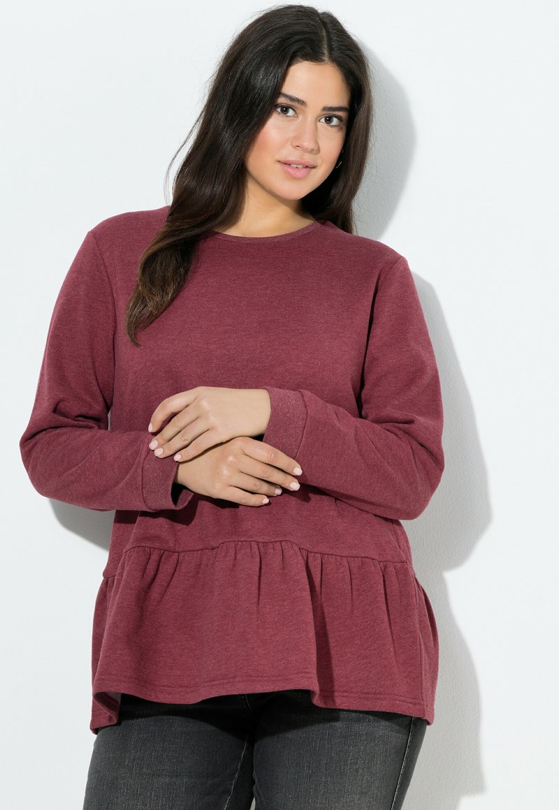 Sudadera burdeos con escote redondo, mangas largas y cintura de peplum. Textura suave y diseño casual, combinada con jeans oscuros.