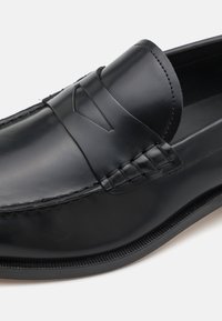Mocassino in pelle nera con una finitura liscia, caratterizzato da una fascia decorativa, cuciture sottili e un design a punta arrotondata.