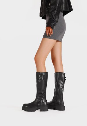 Stivali alti neri in pelle con suola spessa, dettagli con doppia fibbia e chiusura con cerniera laterale. Texture liscia e design resistente.