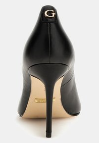 Scarpa nera in pelle con tacco alto e punta affusolata, dotata di un logo in oro "G" sul tacco e una texture liscia e lucida. Dettaglio dorato sulla suola.
