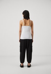 White sleeveless top with thin straps, paired with black cargo pants featuring side pockets, elastic cuffs, and a relaxed fit.