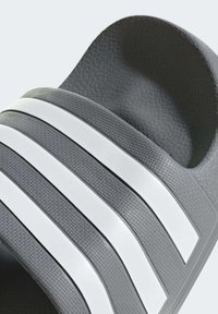 Sandalo grigio a infradito con tre strisce bianche. Presenta un materiale testurizzato e una soletta sagomata per il comfort. Design aperto sulla punta.