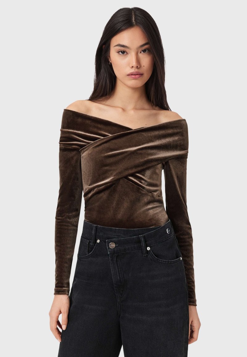 Brun fløjls off-shoulder top med krydset front og lange ærmer, kombineret med højtaljede sorte denimjeans med forlommer.