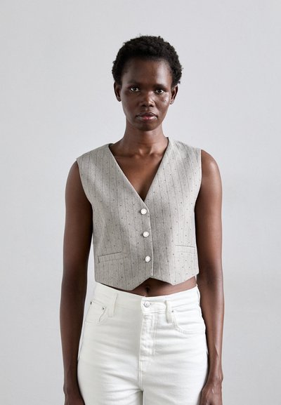 Gilet grigio senza maniche con scollo a V, motivo a righe sottili e tre bottoni frontali, abbinato a jeans bianchi a vita alta.
