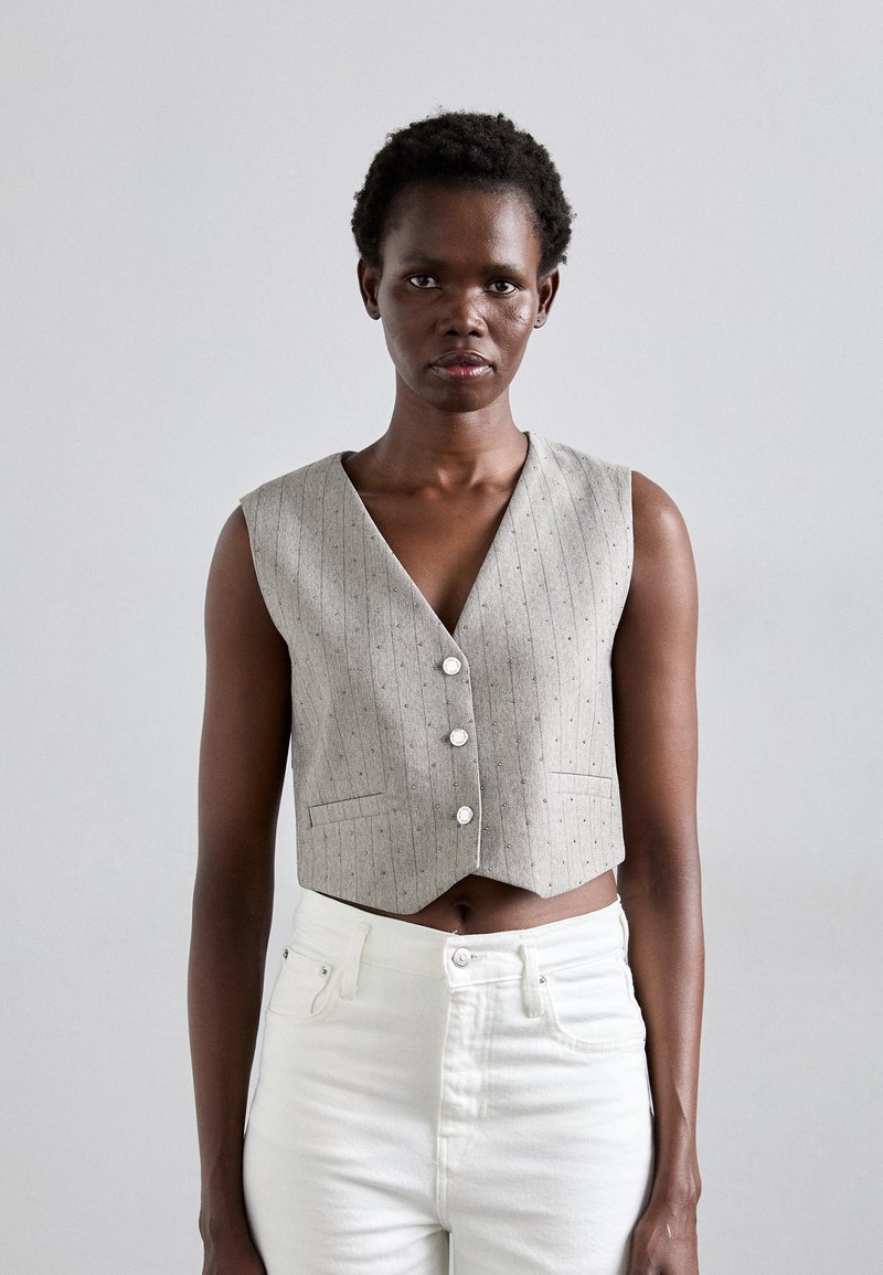 Grå, ärmlös cropped väst med V-hals, randigt mönster och tre framknappar, kombinerad med högmidjade vita jeans.