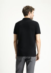 Polo negro de manga corta, hecho de tela suave, con cuello y un diseño limpio. Combinado con pantalones grises, mostrando un aspecto simple y clásico.