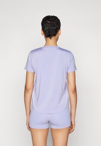 Světle fialový top s krátkými rukávy a kulatým výstřihem, doplněný o odpovídající kraťasy. Látka působí hladce a jemně, s pohodlným volným střihem.