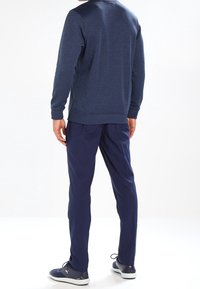 Felpa girocollo blu marina con polsini a costine, abbinata a pantaloni blu marina a gamba stretta e scarpe da ginnastica blu marina, vista da dietro su sfondo bianco.