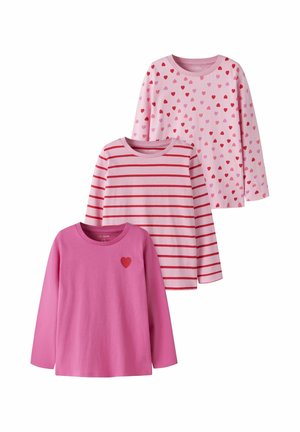 Trois t-shirts à manches longues roses pour enfants, un avec des cœurs rouges et roses, un avec des rayures rouges, et un uni avec un petit cœur rouge sur la poitrine.