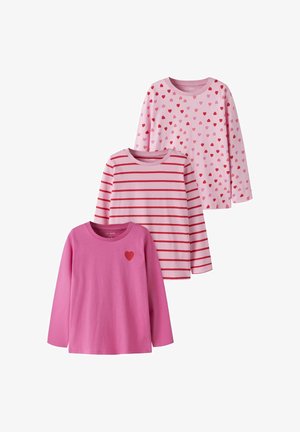 Trois t-shirts à manches longues roses pour enfants, un avec des cœurs rouges et roses, un avec des rayures rouges, et un uni avec un petit cœur rouge sur la poitrine.