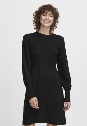 Schwarzes Strickkleid mit tailliertem Oberteil und langen Kabelstrickärmeln. Die Textur ist glatt mit gerippten Akzenten am Halsausschnitt und an den Ärmeln.