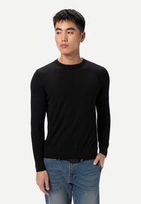 Pull noir à col rond avec une texture lisse, manches longues et coupe ajustée, associé à un jean délavé clair et usé.