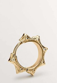 Anillo de oro con acentos texturizados y puntiagudos. Diseño circular que presenta un interior suave y patrones elevados decorativos. Acabado reflectante.