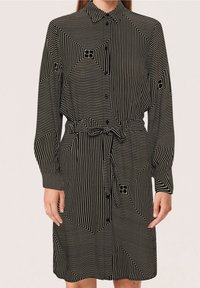 Vestito camicia a righe bianche e nere con colletto, maniche lunghe, chiusura con bottoni davanti, vita con cintura e motivi geometrici sul tessuto.