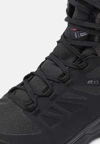 Svart vattentät vintersko med tjocka snören, vadderad krage och texturfodrad överdel för ökad hållbarhet och värme.