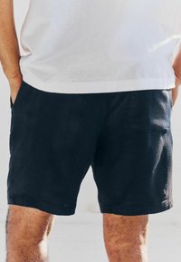 Shorts bleu marine foncé avec un motif texturé, dotés de poches latérales et d'une poche arrière. Fabriqués en tissu doux avec une coupe décontractée.