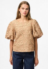 Top beige con texture e maniche corte a sbuffo, con un motivo floreale e un collo rotondo. Abbinato a jeans di denim blu scuro.