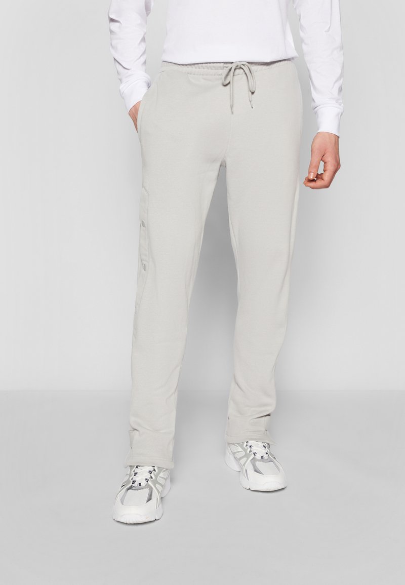 Light gray sweatpants made of soft fabric, featuring a drawstring waist, side pockets, and button details on the legs.