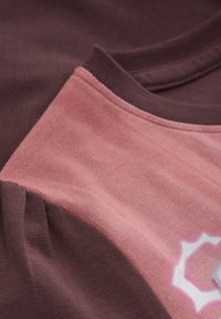 T-shirt en coton avec un design coloré en bourgogne profond et rose doux, avec un col texturé et des détails en impression blanche sur le tissu.