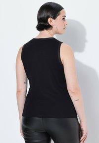 Czarna bezrękawnik z miękkiego materiału o dopasowanym kroju. Posiada okrągły dekolt i gładką teksturę, zestawiony z czarnymi legginsami.