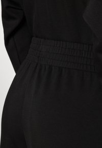 Black garment featuring an elastic waistband with pleated texture. Smooth fabric with a fitted design, emphasizing the waistline.