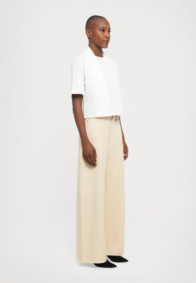 Biely cropped top s krátkymi rukávmi, doplnený o voľné béžové široké nohavice a čierne špicaté topánky. Jednoduchý dizajn, hladký materiál.