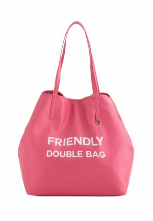 Rosa Tasche aus strukturiertem Material. Sie verfügt über zwei lange Träger und weißen Text mit der Aufschrift "FREUNDLICHE DOPPELTASCHE" auf der Vorderseite.