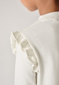 Wit katoenen T-shirt met een gerimpeld accent op de schouder, met een zachte textuur en een eenvoudig ontwerp.