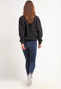 Svart sweatshirt med oversize passform, matchad med mörkblå smala jeans och vita sneakers. Slät tygtextur, avslappnad design.
