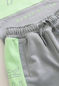 Joggers en verde claro y gris con cinturilla elástica, que cuentan con un cordón, bolsillos laterales y un estampado de marca en la tela.