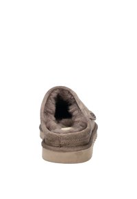 Bruna mockasin med en mjuk, fluffig inredning, rund baksida och en cirkulär logotypdetalj på sidan. Platt, mönstrad sula.