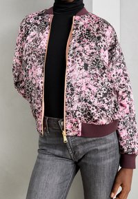 Bloemen bomberjack in roze en zwart, met een ritsluiting, elastische manchetten en een effen murzelfkleurige boord. Gemaakt van lichtgewicht stof.