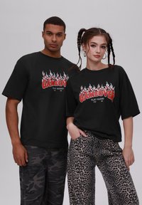 Sorte grafiske t-skjorter med "GAMEOVER" i rødt og flammeakenter. En modell i camobukser, den andre i leopardmønstrede bukser.