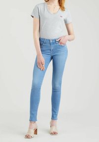 Šedé bavlněné tričko s výstřihem do V v kombinaci se světlými modrými skinny džíny, které mají střední odstín praní a délku ke kotníkům, doplněné hnědými sandály na podpatku.