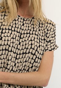 Haut à manches courtes avec un motif de feuilles noires et beiges, confectionné dans un tissu léger à texture lisse.