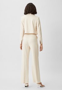 Skuren krämblazer med lång ärm och sprund, parat med vida krämbyxor. Slät textur; minimalistisk design; matchande färg.