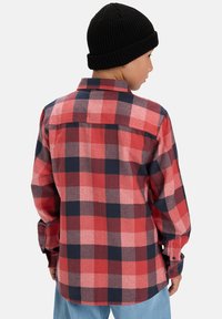 Rood en marineblauw geblokt flanellen overhemd van achteren, met een knoopsluiting, lange mouwen en een gebogen zoom. Gemaakt met een zwarte gebreide beanie.