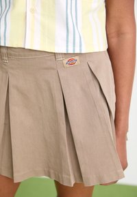 Gonna plissettata color khaki realizzata in tessuto misto cotone, con etichetta del brand Dickies sulla vita e una superficie liscia.