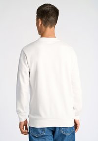 Vit sweatshirt med rund halsringning och långa ärmar, texturerad väv, ribbade muddar och rak fåll, tillsammans med blå jeans.