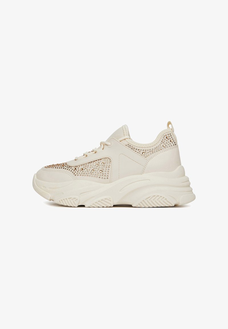 Masywne beżowe sneakersy z metalowymi ćwiekami, teksturowana gumowa podeszwa, zaokrąglony czubek i sznurowane zapięcie. Wykonane z lekkiego syntetycznego materiału.