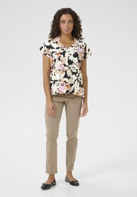 Cvetna majica s kratkimi rokavi na črnem ozadju, okrašena s rožnatimi in belimi cvetovi, v kombinaciji s bež hlačami in črnimi baletkami.