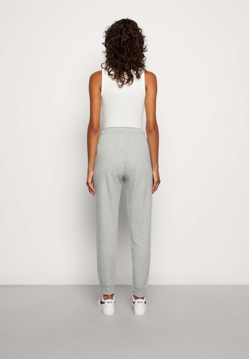 Pantalons de survêtement gris avec une taille élastique, se rétrécissant aux chevilles, associés à un débardeur blanc ajusté et des baskets blanches.