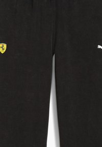 Sorte sweats med blødt stof, med et gult Ferrari-skjoldlogo og et hvidt Puma-logo på siden. Standard pasform, elastisk talje.