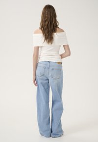 White off-shoulder top with ruched texture paired with light blue wide-leg jeans featuring a leather patch and classic back pockets.