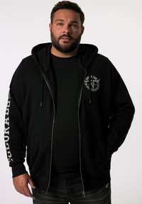 Sudadera negra con cremallera, capucha con cordón, bolsillos laterales y un logo circular en el pecho. Presenta texto blanco a lo largo de una manga.