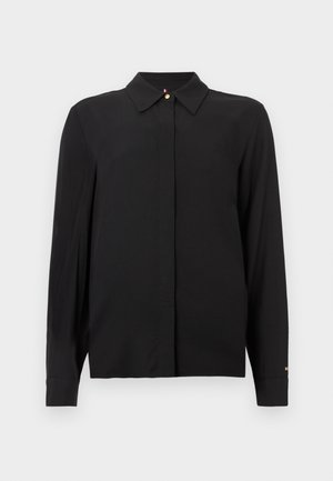 Črna majica z dolgimi rokavi iz gladkega blaga, z ovratnikom, sprednjim zapenjanjem na gumbe in zlato poudarkom na manšetah. Nežen vezen logotip.