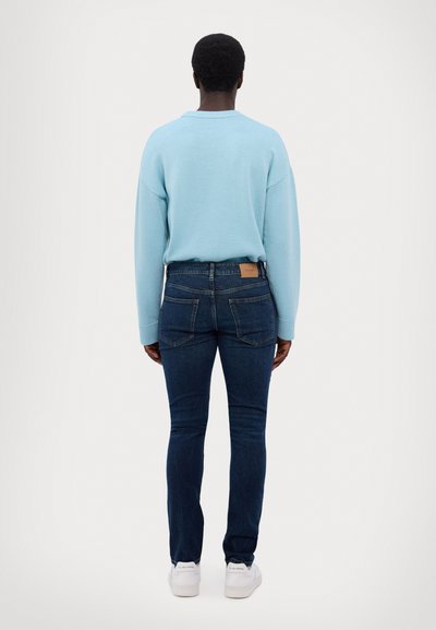 Light blue sweater, slim-fit dark jeans, and white sneakers. Sweater has a round neckline; jeans feature back pockets and a leather tag.