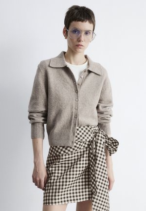 Light brown wool cardigan with a collar, button front, and ribbed cuffs; paired with a black and white checked wrap skirt.